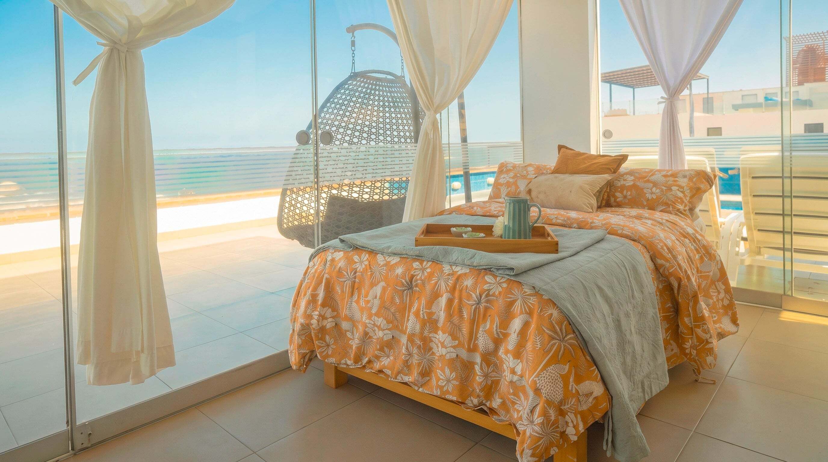 A bedroom with a bed, a hanging chair, and a view of the sea.