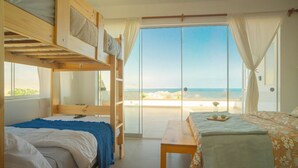 A room with bunk beds, a wooden table, and a view of the beach.