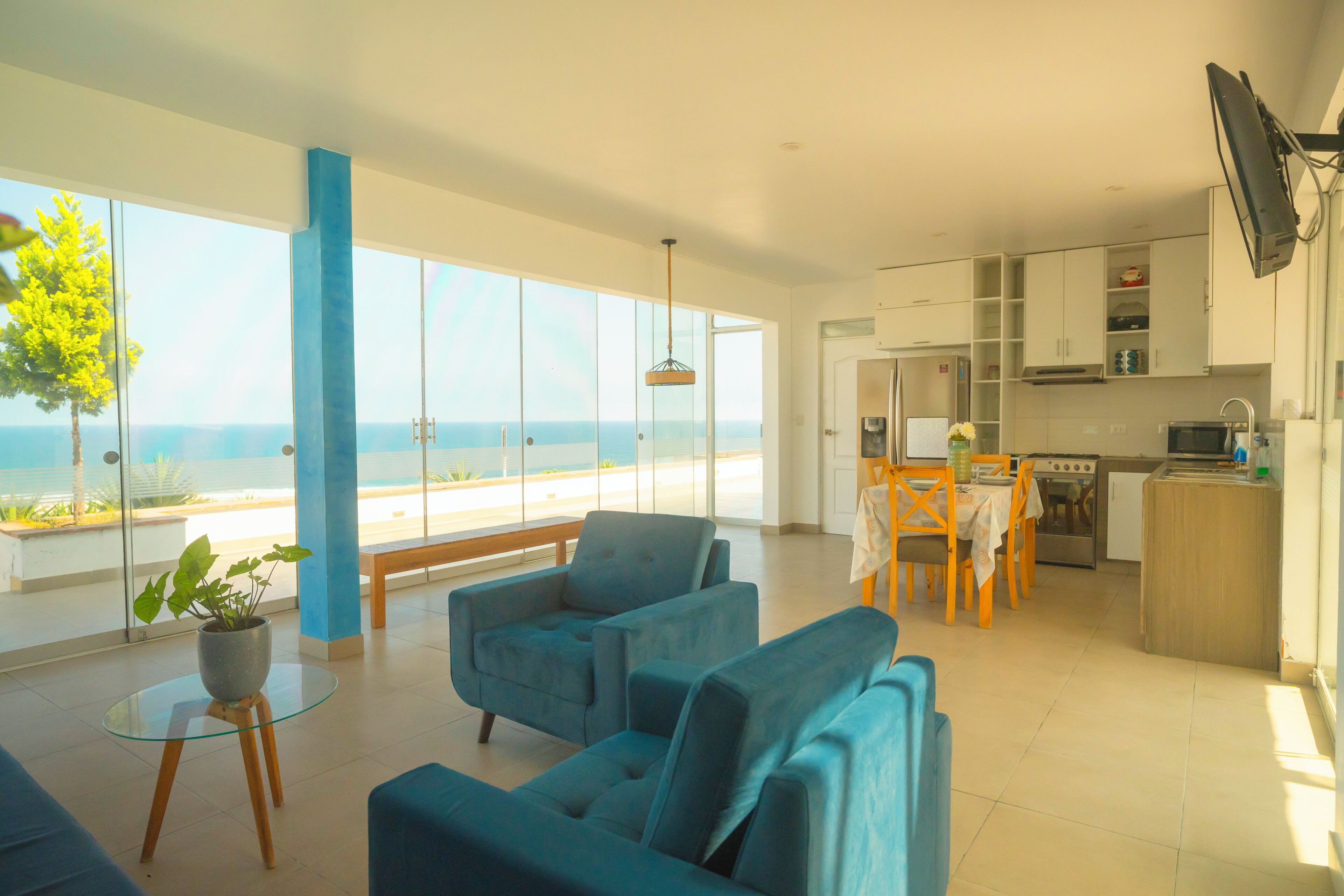 Una sala de estar moderna con vista al mar, un comedor con mesa y sillas, y una cocina equipada.