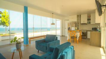 Una sala de estar moderna con vista al mar, un comedor con mesa y sillas, y una cocina equipada.
