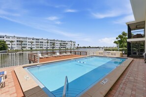 A swimming pool with lounge chairs and a view of a waterfront building. - Brightwater Beach Condo | Bay Views & Beach Access (St. Petersburg)