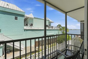 A balcony with a view of a body of water, a building with a light blue exterior, and a covered outdoor seating area. - Brightwater Beach Condo | Bay Views & Beach Access (St. Petersburg)