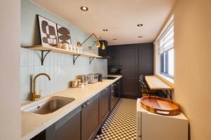 Una cocina con piso de cuadros, un lavamanos, una encimera con diversos objetos y un ventanal que proporciona luz natural.