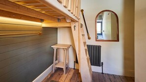 En trætrap fører op til et soveværelse på loftet, med et indbygget skrivebord og en radiator nedenunder.