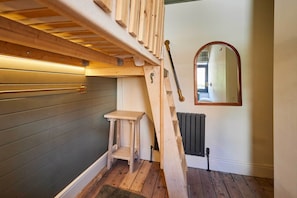 Eine Holztreppe führt zu einem Schlafzimmer auf dem Dachboden, mit integriertem Schreibtisch und Heizkörper darunter.