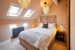 Ein Schlafzimmer mit einem großen Bett, zwei Nachttischlampen, einem dekorativen Kopfteil und Dachfenstern.