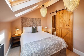 Un dormitorio con una cama grande, dos mesitas de noche con lámparas, un cabecero decorativo, un armario de madera y un tragaluz.