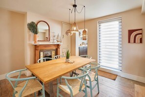 A dining area with a wooden table and light blue chairs, a fireplace, and hanging pendant lights. - Host & Stay | Casa Formentera (Scarborough)
