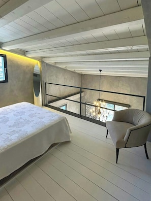 Ein Schlafzimmer mit einem großen Bett, einem Sessel, einem Balkon mit Blick und einer Chandelier.