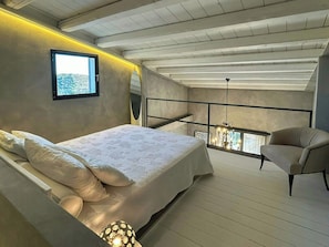 Ein Schlafzimmer mit Bett, Sessel, Fenster und Balkon mit Geländer.