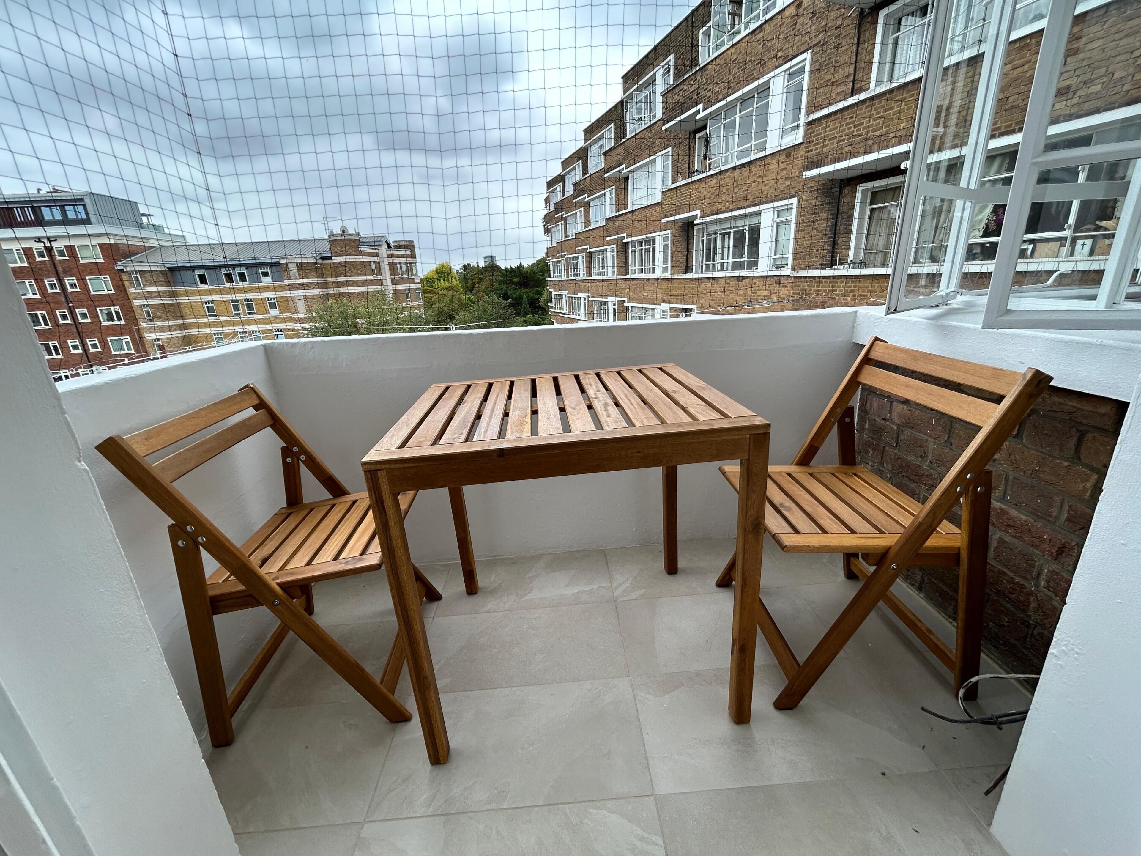 Un balcon avec une table et des chaises en bois, une vue sur un bâtiment en briques et un sol carrelé.