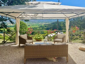 A covered outdoor seating area with wicker furniture and potted plants, overlooking a scenic landscape. - Stone cottage with view of Gubbio and shared pool (Gubbio)