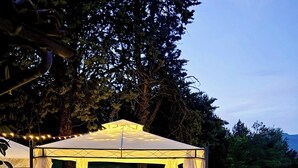 A gazebo with a gravel floor and white furniture, surrounded by trees and potted plants. - Stone cottage with view of Gubbio and shared pool (Gubbio)