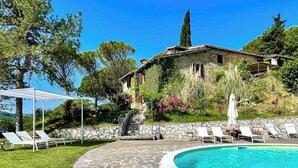A swimming pool with lounge chairs, a stone pathway, and a building with a stone facade and vegetation. - Stone cottage with view of Gubbio and shared pool (Gubbio)