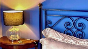 A bed with white and striped pillows, a blue headboard, and a lamp on a wooden side table. - Stone cottage with view of Gubbio and shared pool (Gubbio)