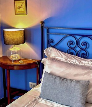 Ein Bett mit weißen und gestreiften Kissen, einem blauen Kopfteil und einer Lampe auf einem Holznachttisch.