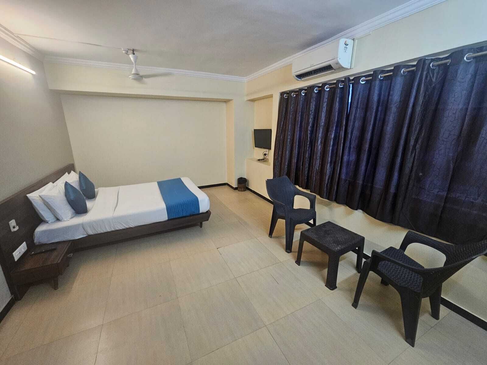Een kamer met een bed, twee stoelen, een tafeltje, een airconditioning en een plafondventilator.