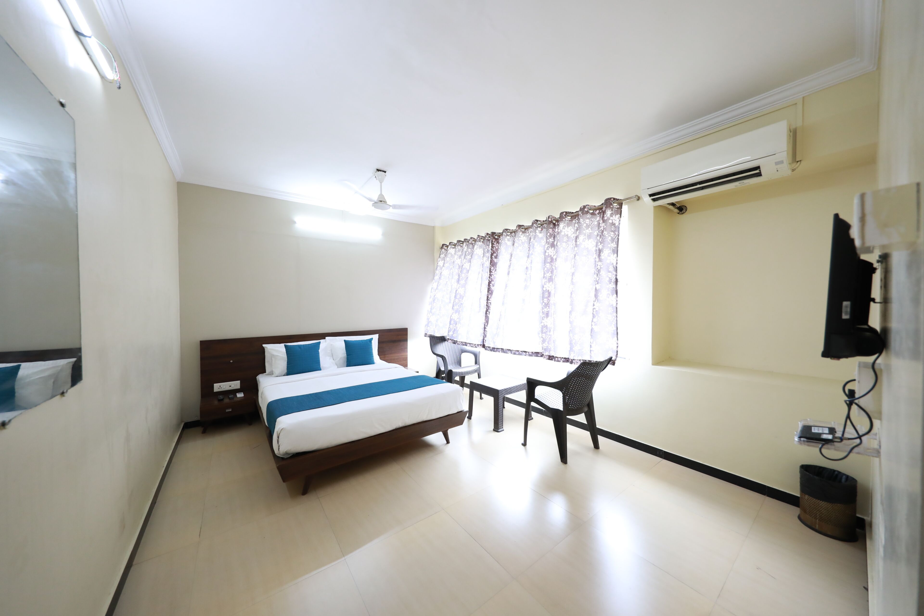 A hotel room with a bed, a desk, a chair, an air conditioning unit, and a window with curtains.