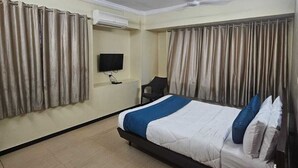 A hotel room with a bed, curtains, a ceiling fan, a TV, and a chair. - Hotel Alt Acco close to Kharadi (Pune)