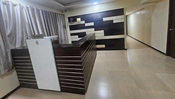 A reception area with a counter, a ceiling fan, and a wall with a geometric pattern. - Hotel Alt Acco close to Kharadi (Pune)