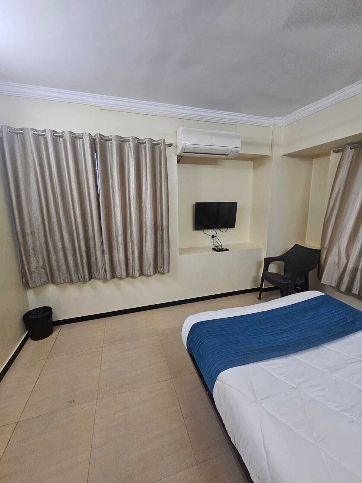 Ein Hotelzimmer mit Bett, Vorhängen, einer Klimaanlage, einem Fernseher und einem Mülleimer.
