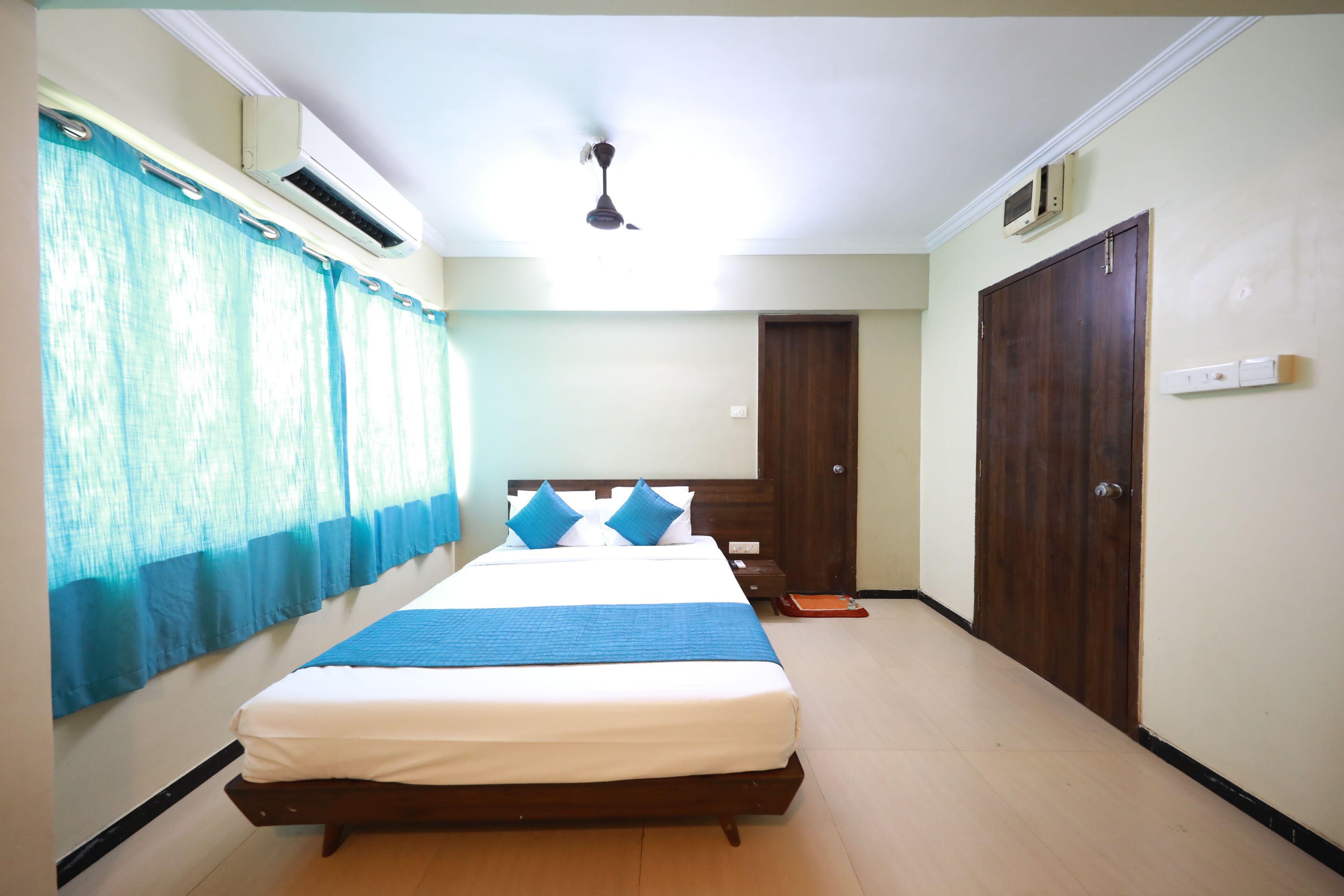 A bedroom with a large bed, a ceiling fan, an air conditioning unit, and a wardrobe.