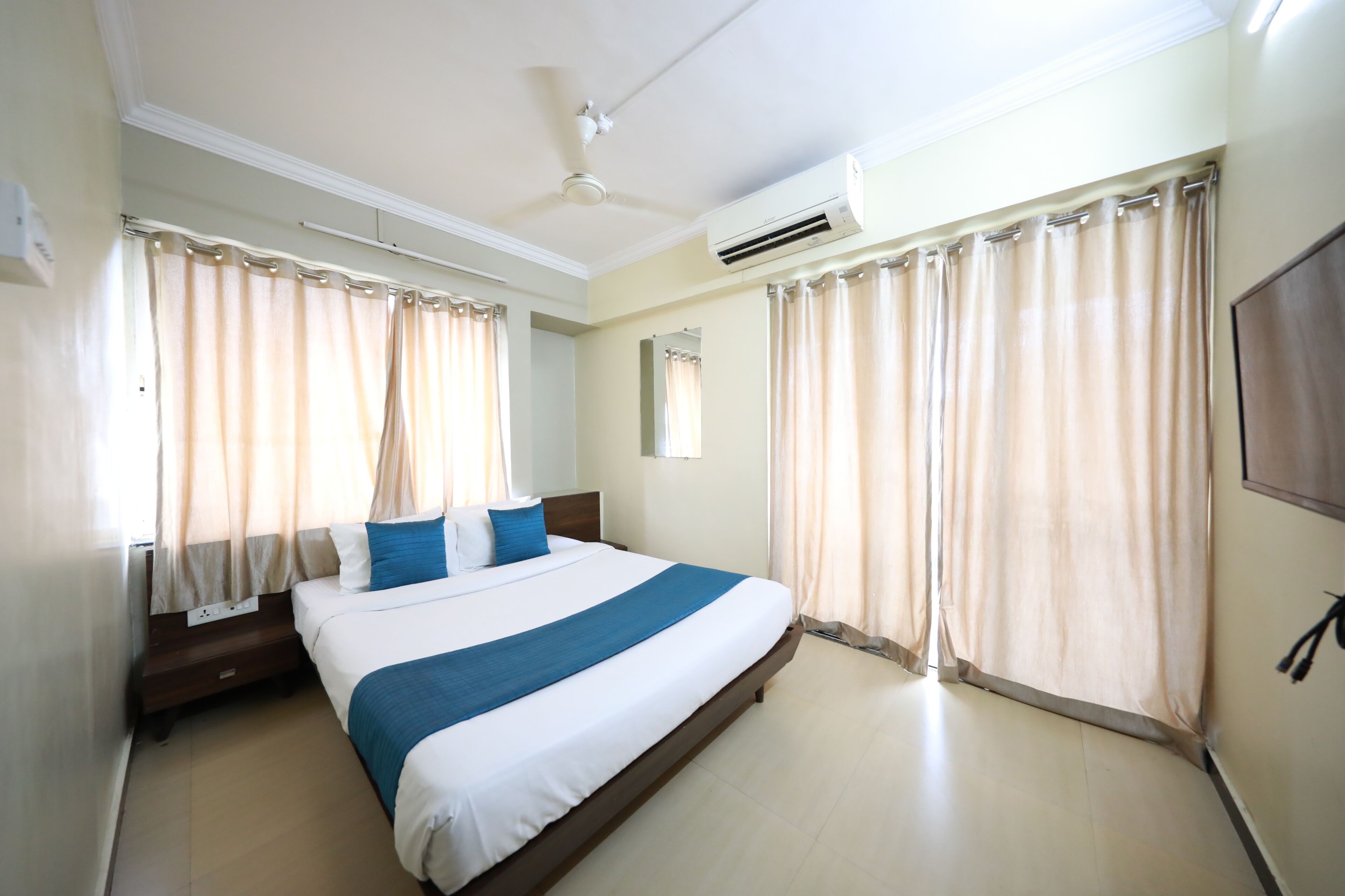 A hotel room with a large bed, curtains, an air conditioning unit, and a ceiling fan.
