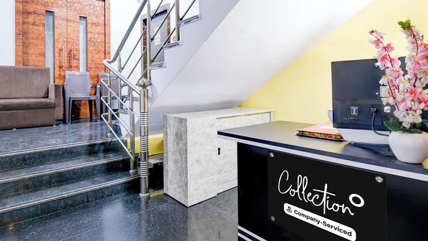 A modern reception desk with a logo, a staircase, a sofa, and a decorative plant. - Collection O Shyam Bazar Metro Station (Kolkata)