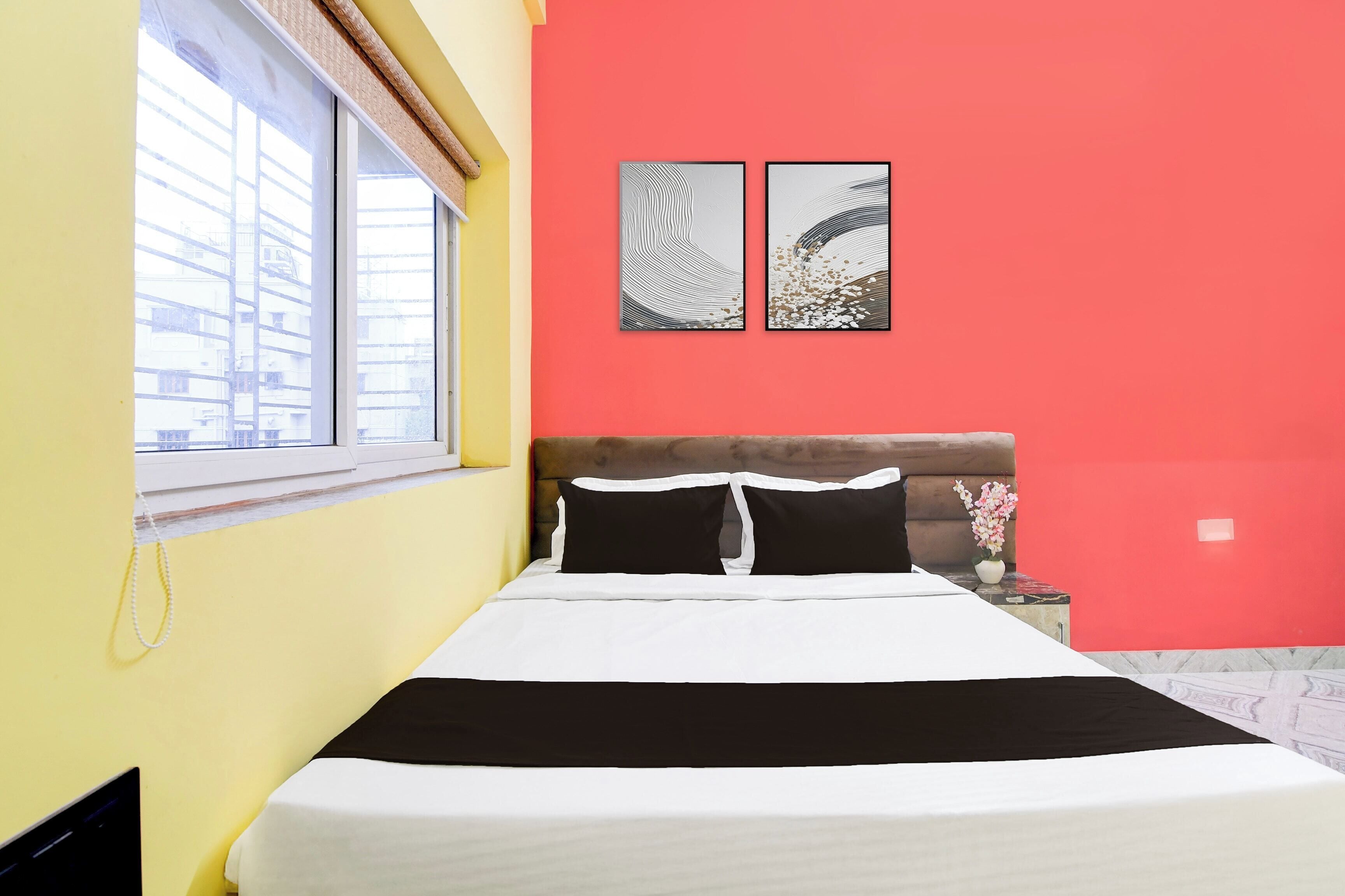 Ein Bett mit schwarz-weißer Bettwäsche, ein Fenster mit Jalousien und zwei an der Wand befestigte Kunstwerke.