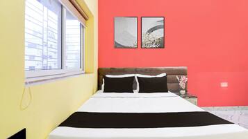 Ein Bett mit schwarz-weißer Bettwäsche, ein Fenster mit Jalousien und zwei an der Wand befestigte Kunstwerke.