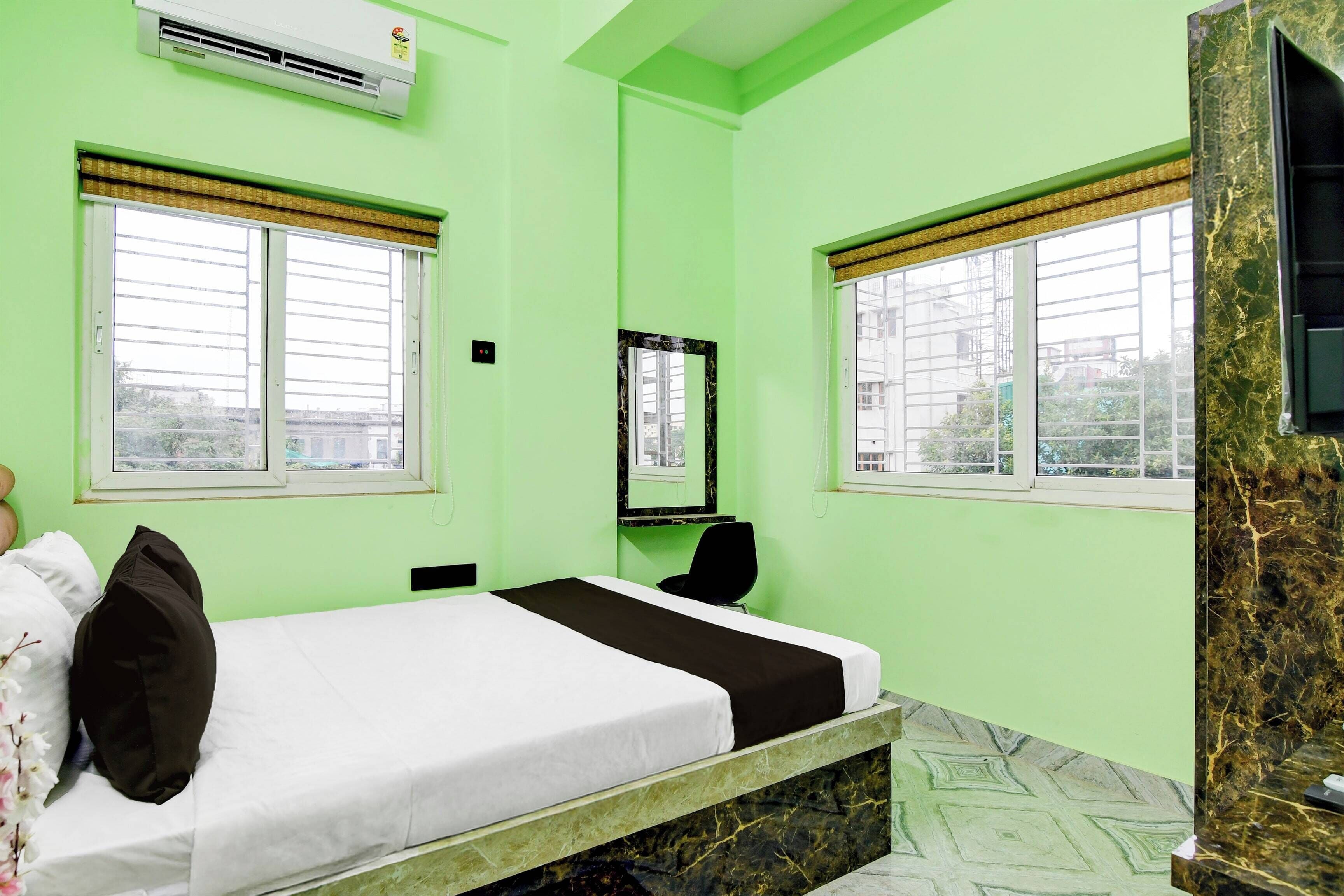 Um quarto com cama, poltrona, espelho e janela com vista para edifícios.