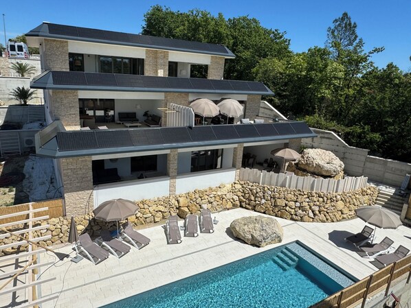 Et moderne hus med to etager, swimmingpool, udendørs møbler og solpaneler.