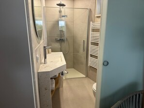 Et moderne badeværelse med brusekabine i glas, vask med håndklædestang og toilet.