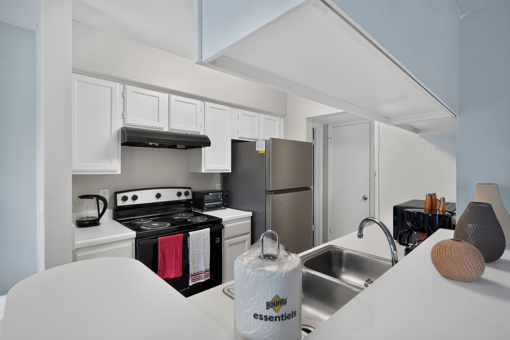 A modern kitchen with white cabinets, a stainless steel refrigerator, a black stove, and a sink with a faucet.
