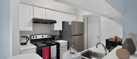 A modern kitchen with white cabinets, a stainless steel refrigerator, a black stove, and a sink with a faucet.