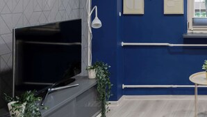 A modern living room with a flat-screen TV, a white floor lamp, and decorative plants. - Unique Studio for 2 Persons | Pet Friendly (Warszawa)