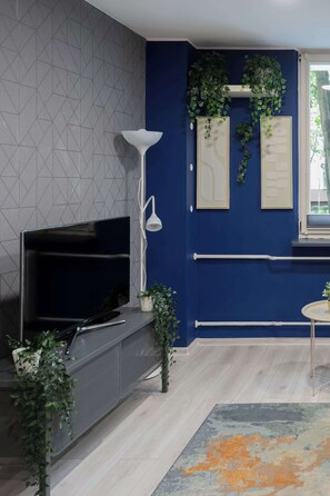Ein modernes Wohnzimmer mit einem Flachbildfernseher, einer weißen Stehlampe und Zimmerpflanzen.