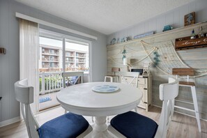 Ein Zimmer mit einem runden Tisch, zwei Stühlen, Blick auf einen Balkon mit einem Gebäude und einem Regal mit Dekoration.