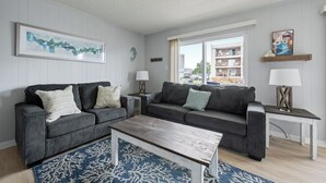 Ein Wohnzimmer mit zwei grauen Sofas, einem Holztisch und einem blauen Teppich mit Muster.