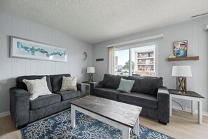 Ein Wohnzimmer mit zwei grauen Sofas, einem Holztisch und einem blauen Teppich mit Muster.