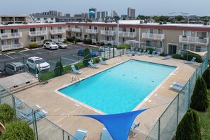 Ein Swimmingpool mit Liegestühlen und einem Zaun, umgeben von mehrstöckigen Gebäuden.