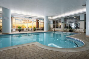 An indoor swimming pool with a view of the sunset through large windows, surrounded by lounge chairs and potted plants. - Three bedroom oceanfront condo in the luxurious Gateway Grand! (Ocean City)