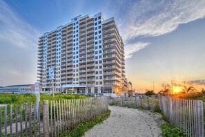 A high-rise hotel with multiple balconies, a sandy pathway leading to the entrance, and a sunset in the background. - Three bedroom oceanfront condo in the luxurious Gateway Grand! (Ocean City)