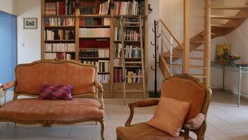 Une pièce comprenant deux fauteuils richement décorés, une grande bibliothèque et un escalier en bois.