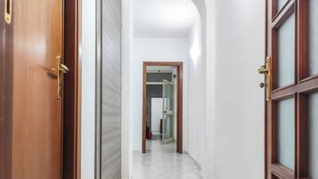 A corridor with a wooden door on the left, a white wall on the right, and a glass door at the end.