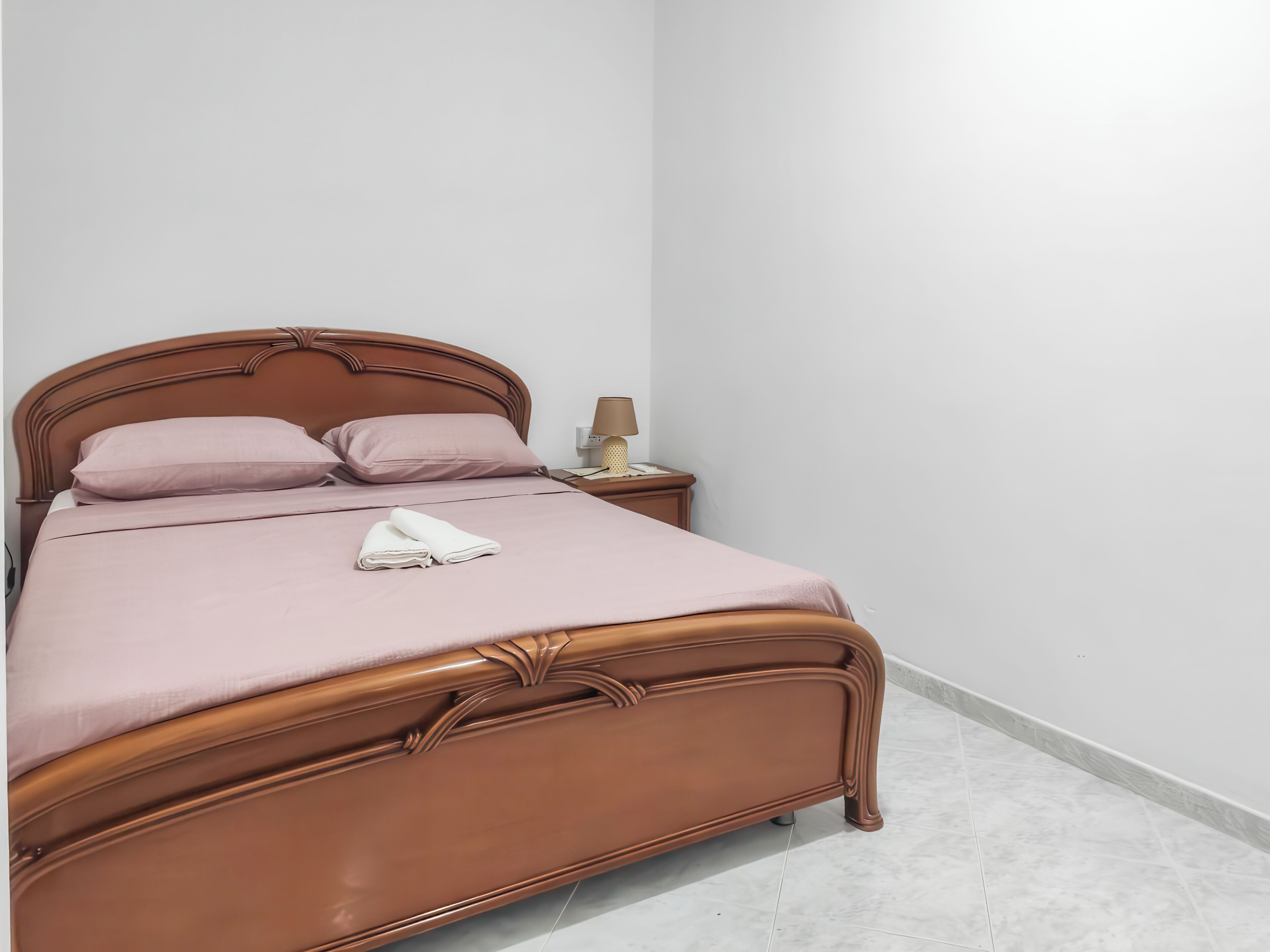 Un lit bien fait, avec une tête de lit, une table de chevet avec une lampe et un interrupteur fixé au mur.