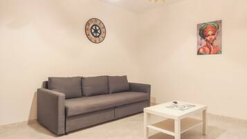 A modern living room with a grey sofa, a white coffee table, a wall clock, and a framed artwork.
