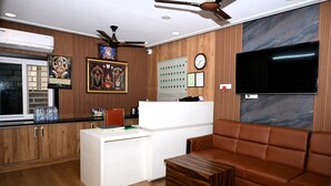 Una cocina moderna con encimera blanca, armarios de madera, ventilador de techo y un televisor de pantalla plana grande montado en la pared.