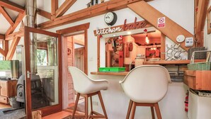 A kitchen with a 'kitchen bake' sign, wooden beams, a clock, and two white bar stools. - Cool Cabin (Leek)