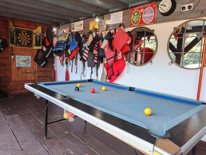 A pool table with balls, a dartboard, and life jackets hanging on the wall. - Cool Cabin (Leek)